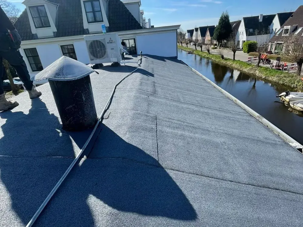Plat dak met nieuwe bitumen dakbedekking langs een sloot met woningen in Westzaan