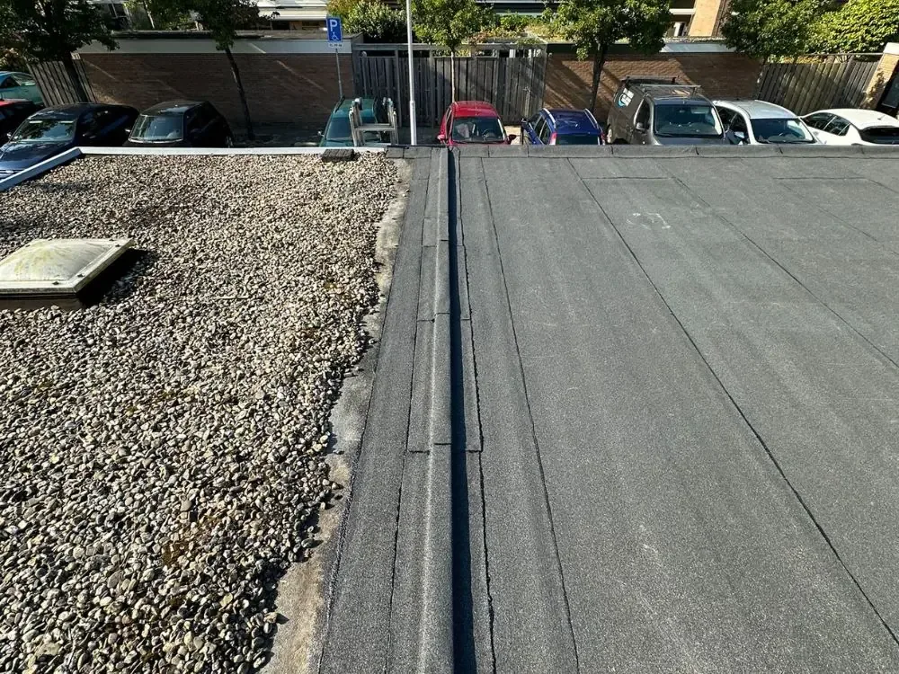 Nieuwe bitumen dakbedekking die aansluit op een grinddak met lichtkoepel in Westzaan