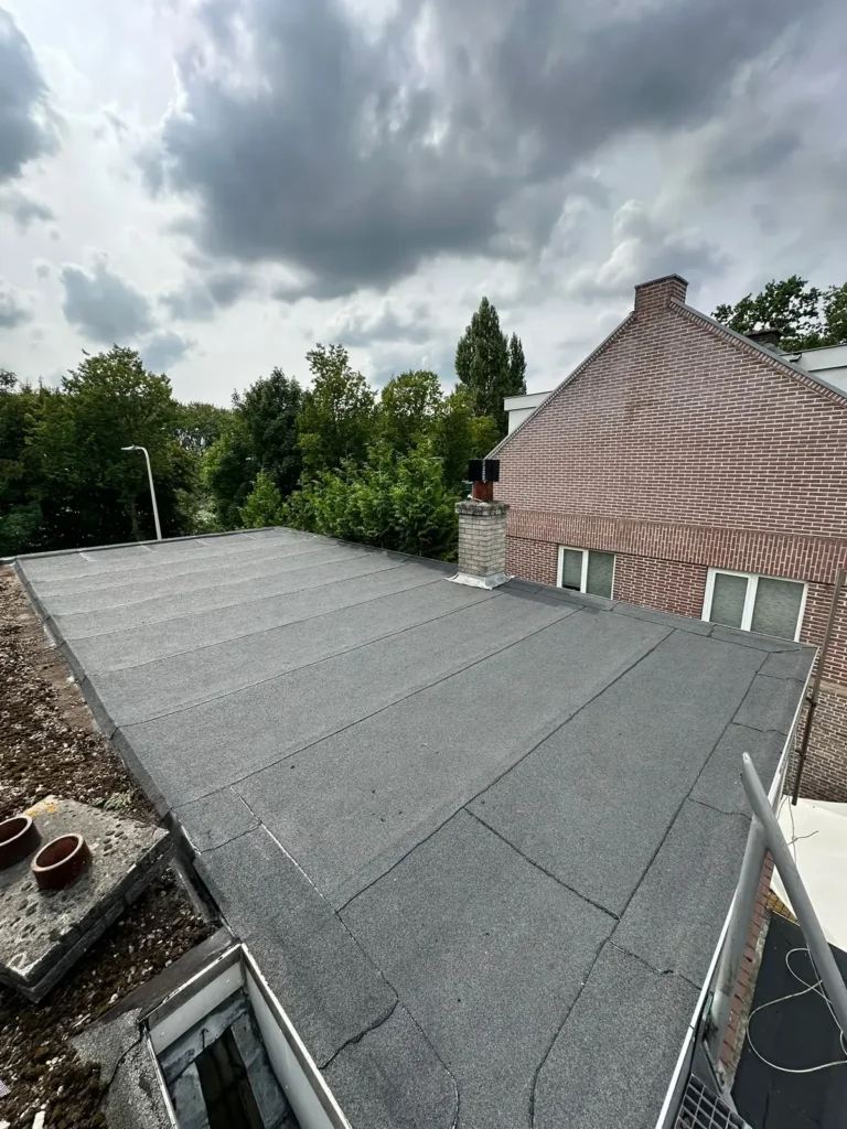 Nieuw bitumen dak naast een bakstenen woning onder een donkere wolkenlucht in Bentveld
