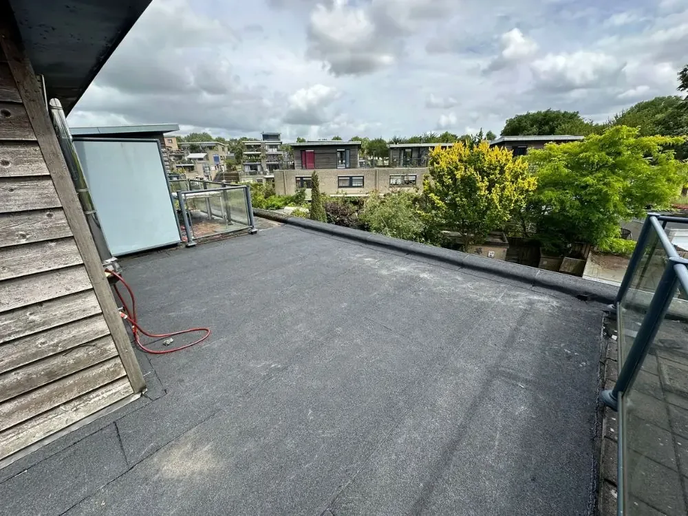 Bitumen dakbedekking op een plat dak naast een dakterras met glazen balustrade in Westzaan