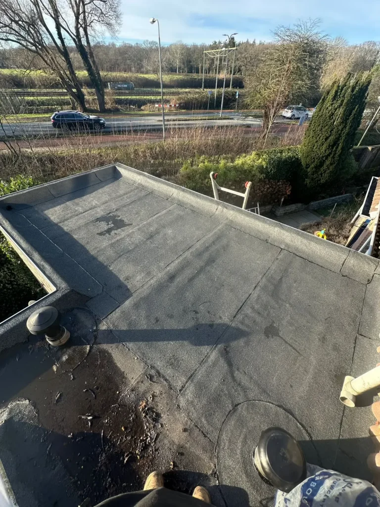 Bitumen dakbedekking met een dakdoorvoer op een plat dak, weg op de achtergrond in Westzaan