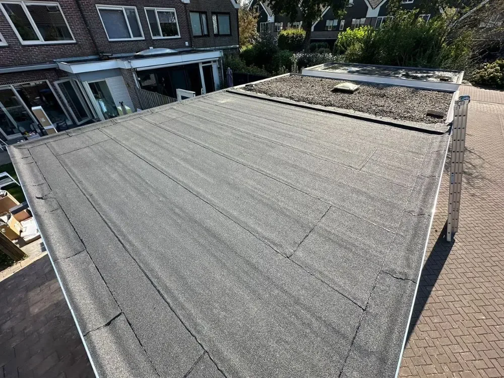 Nieuwe bitumen dakbedekking op een plat dak achter een woning in Westzaan
