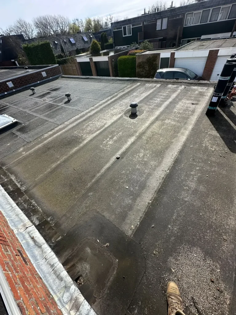 Verouderd plat garagedak met groene aanslag en een dakdoorvoer in Heemskerk
