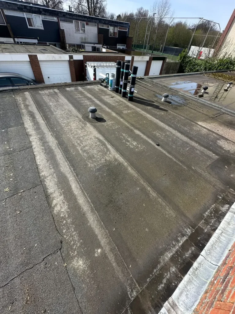 Oud plat garagedak met rollen bitumen, garageboxen op de achtergrond in Uitgeest