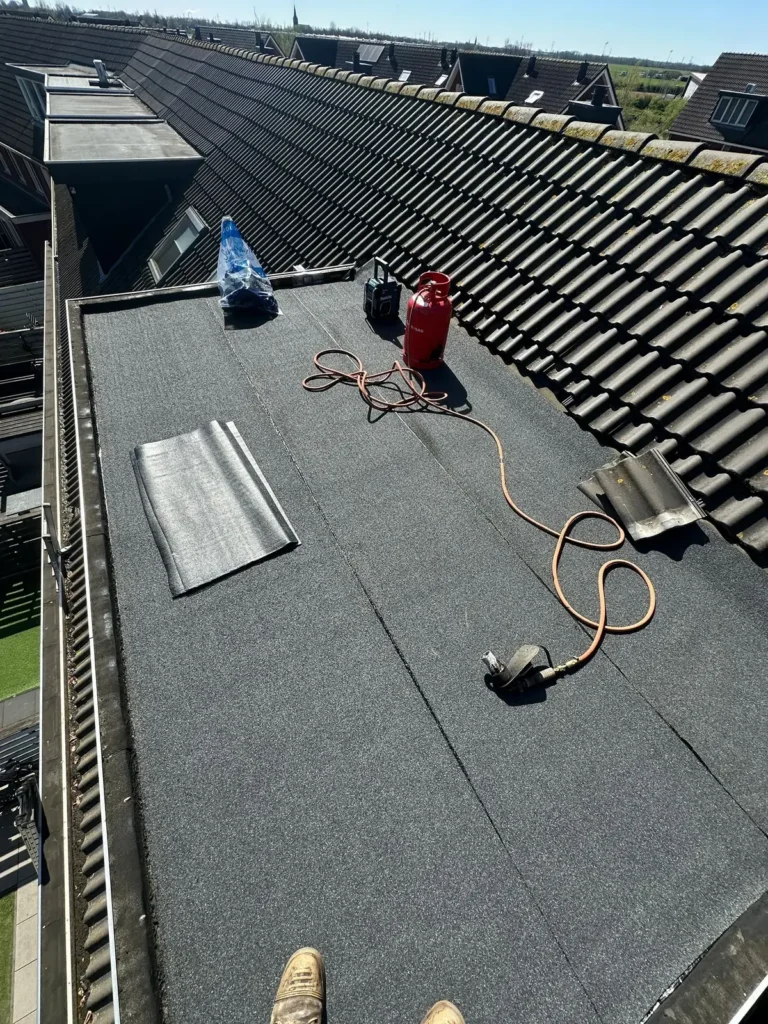 Nieuwe bitumen dakbedekking op een dakkapel, met gasfles en brander op het dak in Velsen