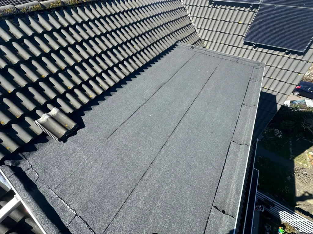 Plat dak van een dakkapel met nieuwe bitumen dakbedekking tussen dakpannen in Velserbroek
