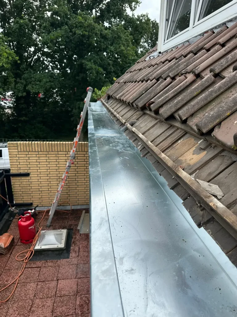 Nieuwe zinken dakgoot naast een pannendak boven een dakterras in Wijk Aan Zee