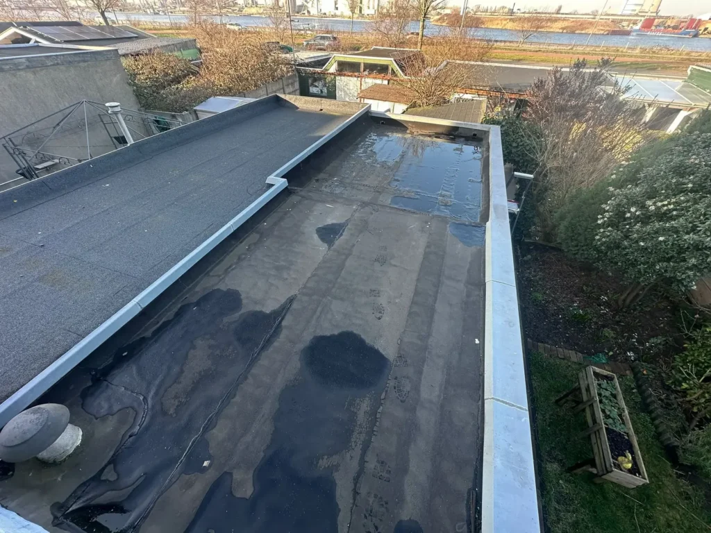 Plat dak met oude natte dakbedekking naast een nieuw bitumen dakvlak in Wormer