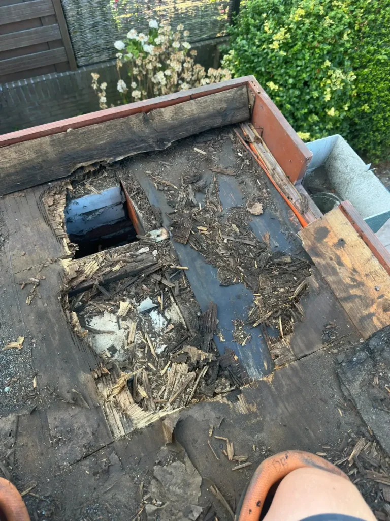 Gat in het verrotte dakbeschot van een plat dak met losse houtresten in Zandvoort