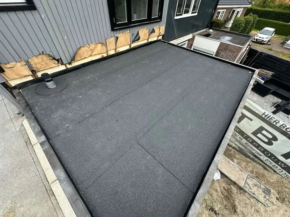 Nieuw bitumen dak op een uitbouw tegen een gevel met houten gevelbekleding in Zandvoort