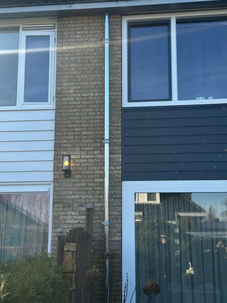 Nieuwe zinken regenpijp met beugels langs de gevel van een woning in Westzaan