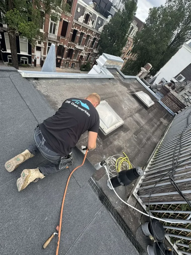 Dakdekker in bedrijfskleding werkt geknield op een plat dak met lichtkoepels in Westzaan