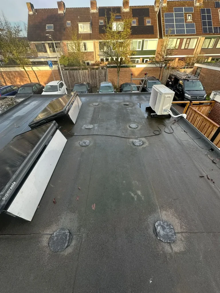 Plat dak met herstelde plekken in de dakbedekking naast zonnepanelen in Westzaan