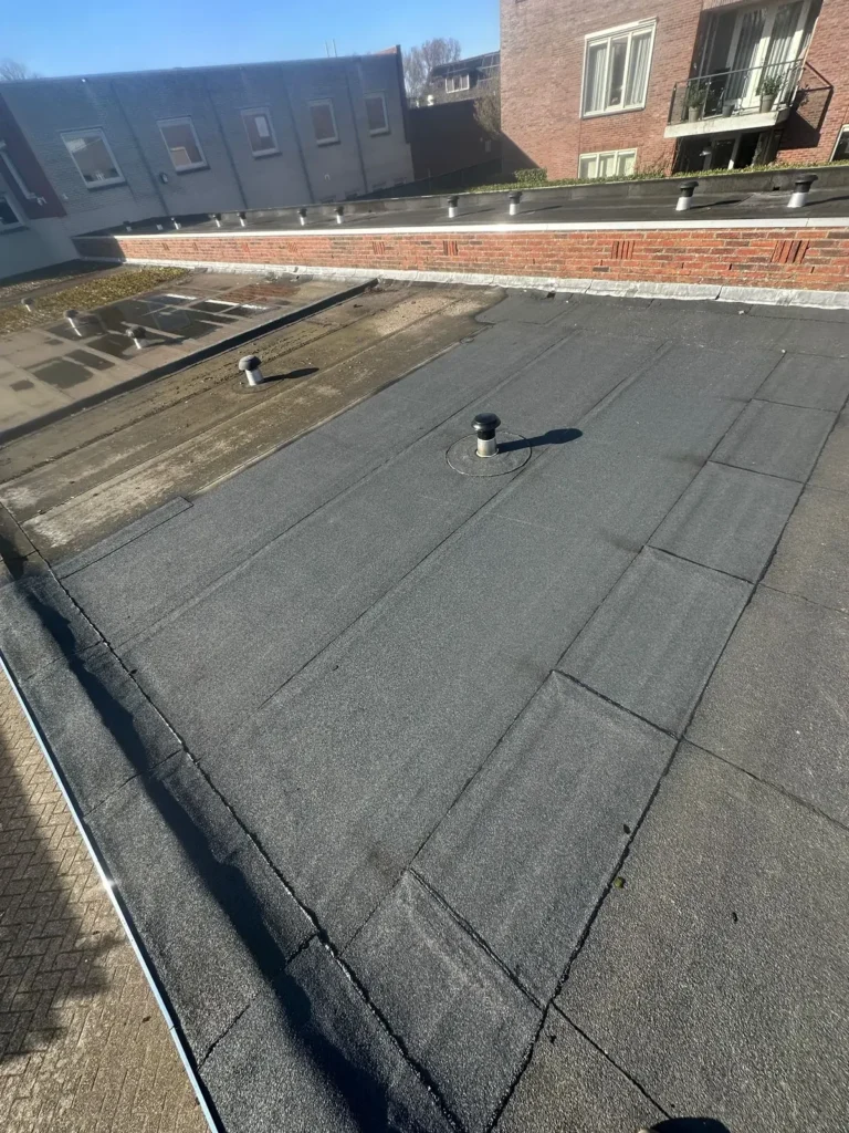 Plat garagedak met nieuwe bitumen dakbedekking rond een dakdoorvoer in Westzaan