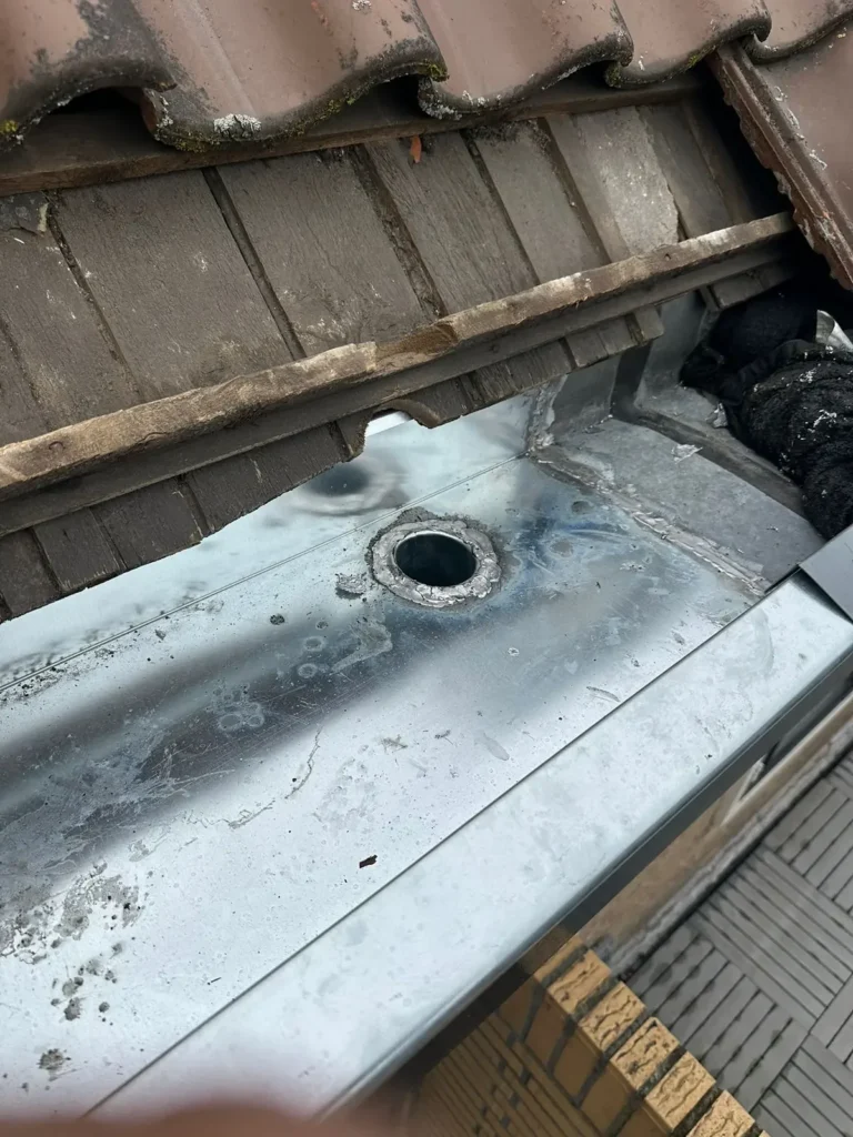 Nieuwe zinken goot met gesoldeerde afvoer onder de dakpannen in Westzaan