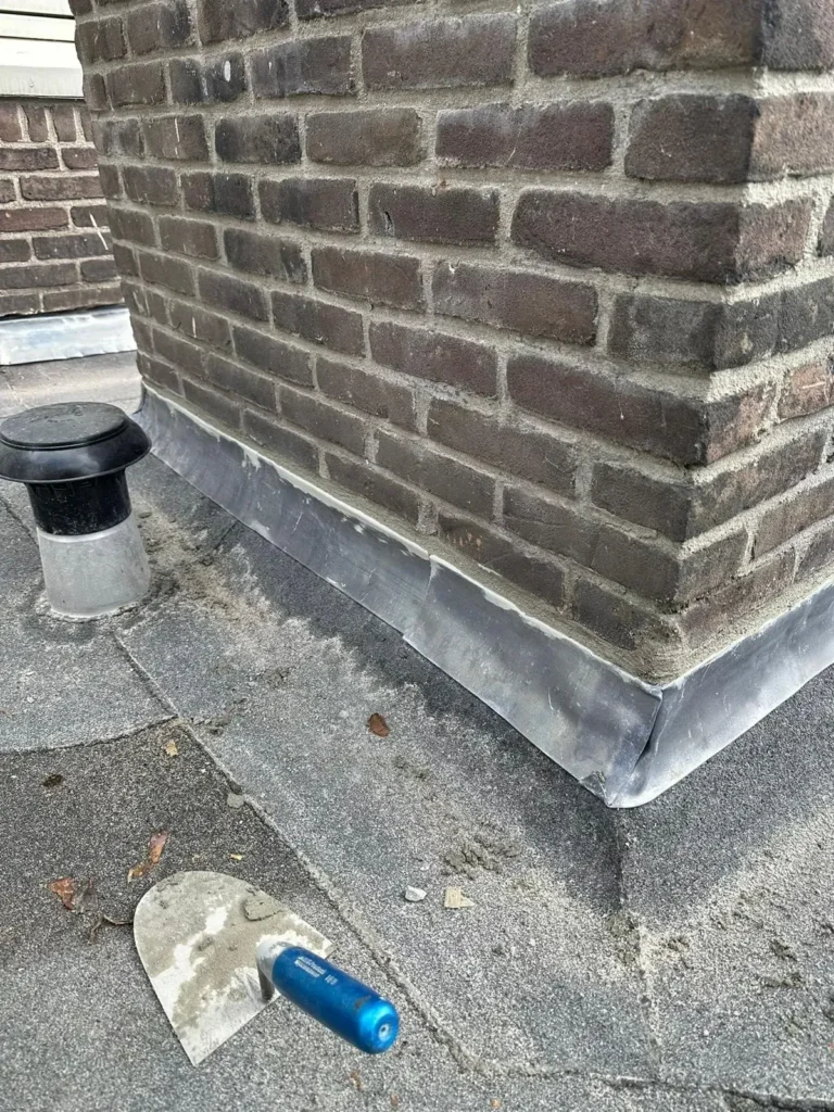 Nieuwe loodslabbe rond de voet van een gemetselde schoorsteen op een plat dak in Westzaan