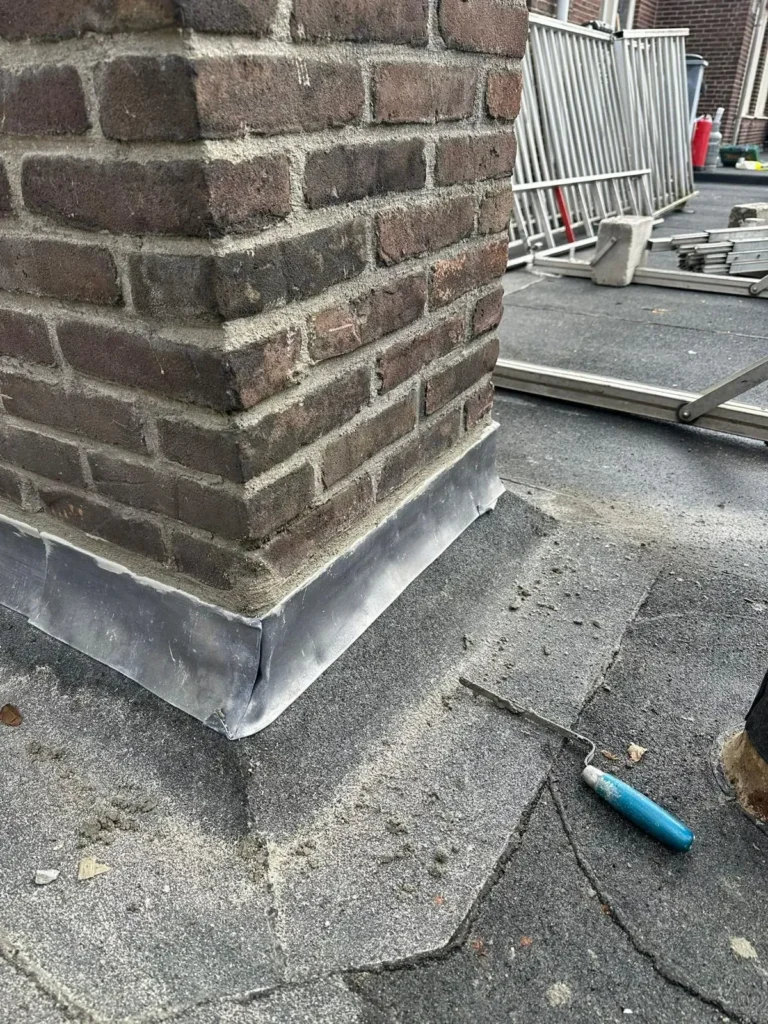 Gemetselde schoorsteen met nieuw loodwerk aan de voet op een plat dak in Westzaan