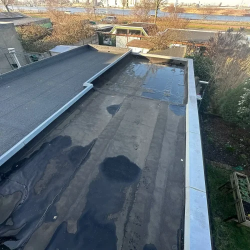 Plat dak met oude natte dakbedekking naast een nieuw bitumen dakvlak in Assendelft
