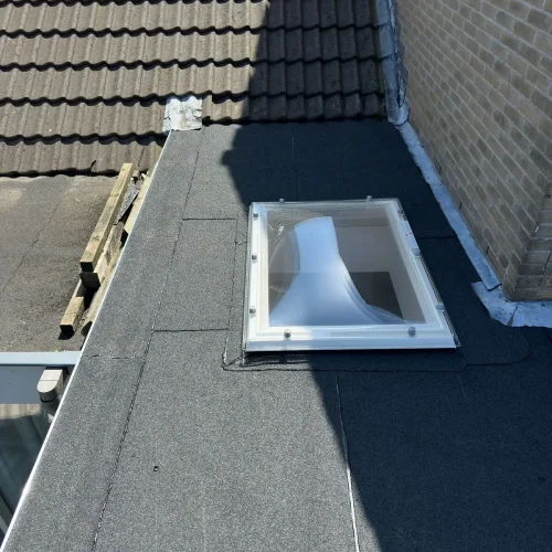 Nieuwe lichtkoepel in een bitumen dak tegen een pannendak en een bakstenen gevel in Bentveld