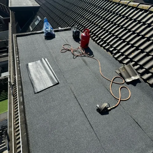 Nieuwe bitumen dakbedekking op een dakkapel, met gasfles en brander op het dak in Heemskerk