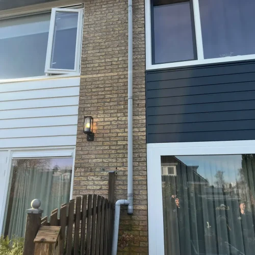Grijze regenpijp met versprongen bocht langs een bakstenen gevel in Krommenie