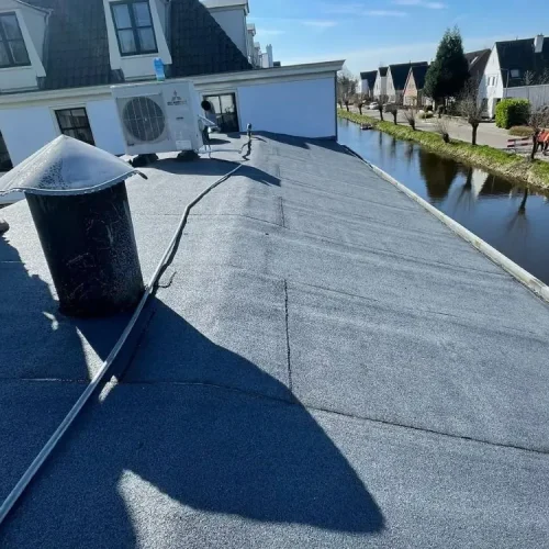 Plat dak met nieuwe bitumen dakbedekking langs een sloot met woningen in Velserbroek