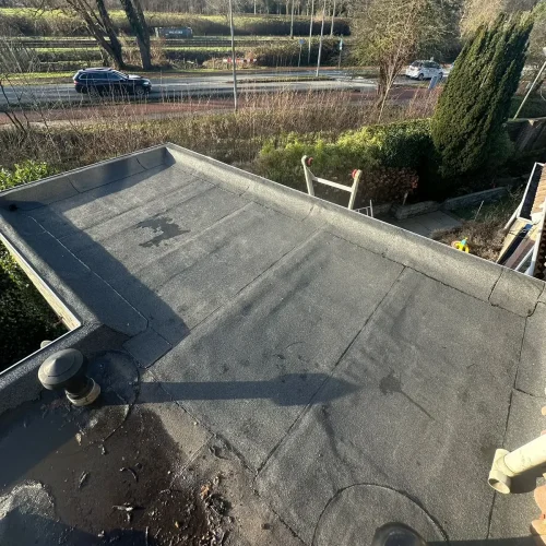 Bitumen dakbedekking met een dakdoorvoer op een plat dak, weg op de achtergrond in Velserbroek