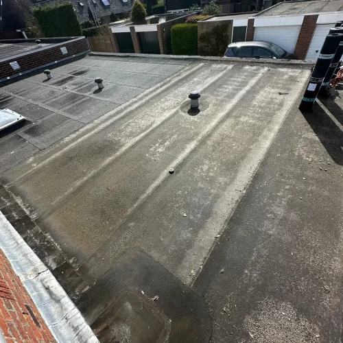 Verouderd plat garagedak met groene aanslag en een dakdoorvoer in Wormer