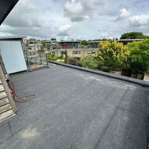 Bitumen dakbedekking op een plat dak naast een dakterras met glazen balustrade in Zaandam
