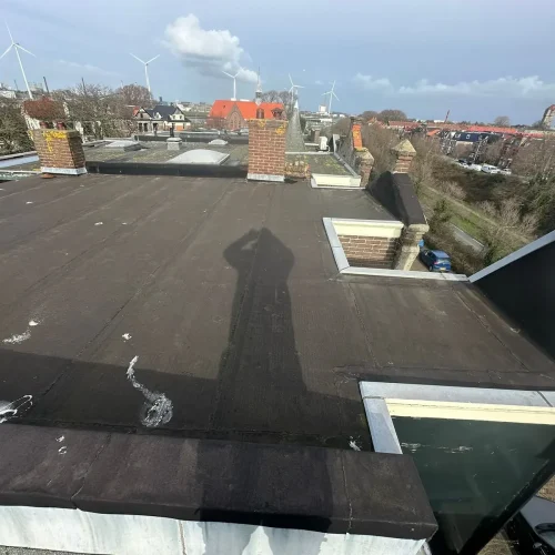 Oud bitumen dak met schoorstenen en uitzicht over daken en windmolens in Zandvoort